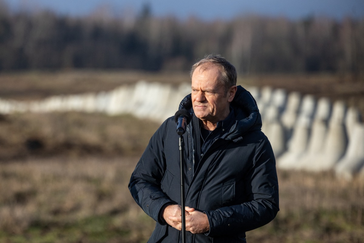 Poland's Prime Minister Donald Tusk speaks with concrete anti-tank barriers in the background during his inspection of the first completed section of fortifications 