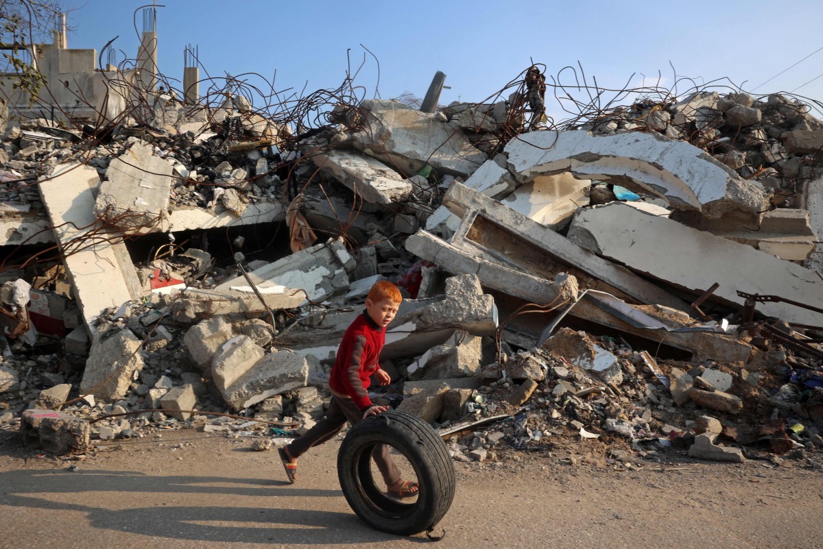  A boy plays with a rubber tyre next to the rubble of buildings destroyed in Israeli airstrikes near the Nuseirat refugee camp in the central Gaza Strip on January 11, 2025. (Photo by Eyad BABA / AFP)
