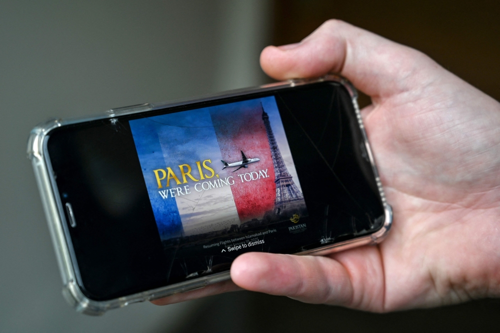 A man looks at an advert of the Pakistan International Airlines (PIA) plane flying at the Eiffel Tower, on his mobile phone in Islamabad on January 17, 2025. (Photo by Farooq Naeem / AFP)
