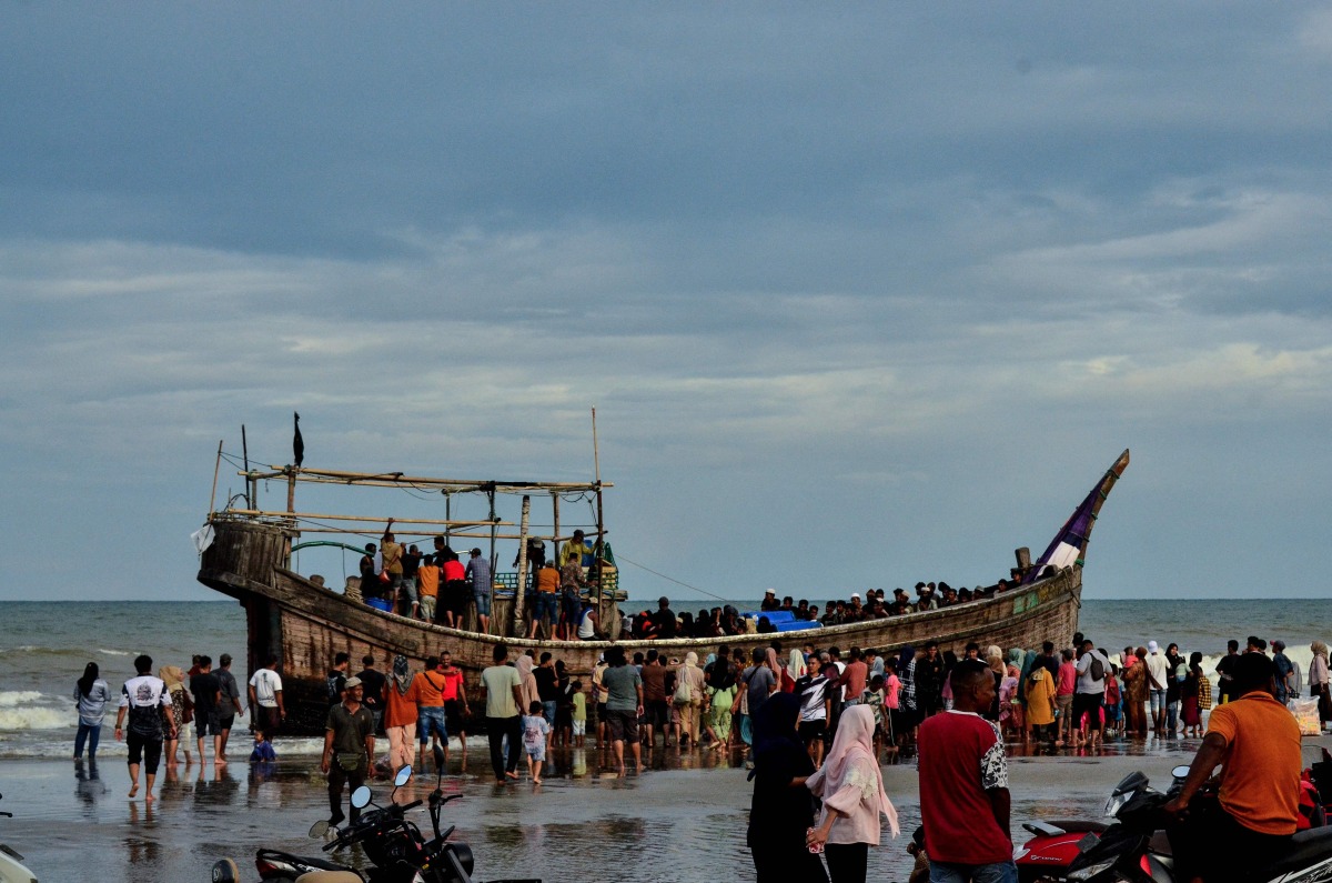 People gather around a boat carrying newly-arrived Rohingya refugees, after authorities prevented the refugees from disembarking and ordered them to remain on board the vessel, at Leuge Beach in Indonesia's Aceh province on January 29, 2025. (Photo by Cek MAD / AFP)
