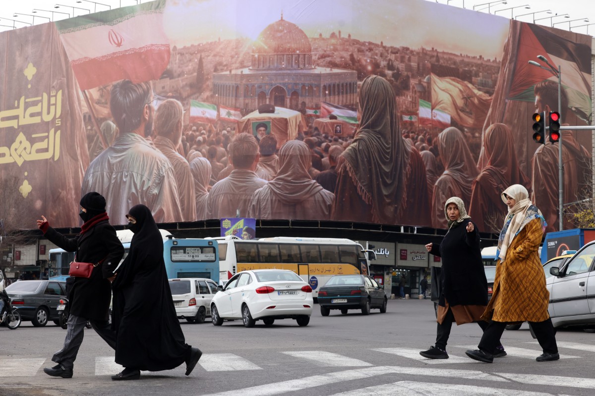 Women walk in front of a banner covering the facade of a building in Tehran, hours before his funeral in Beirut on February 23, 2025. (Photo by Atta Kenare / AFP)
