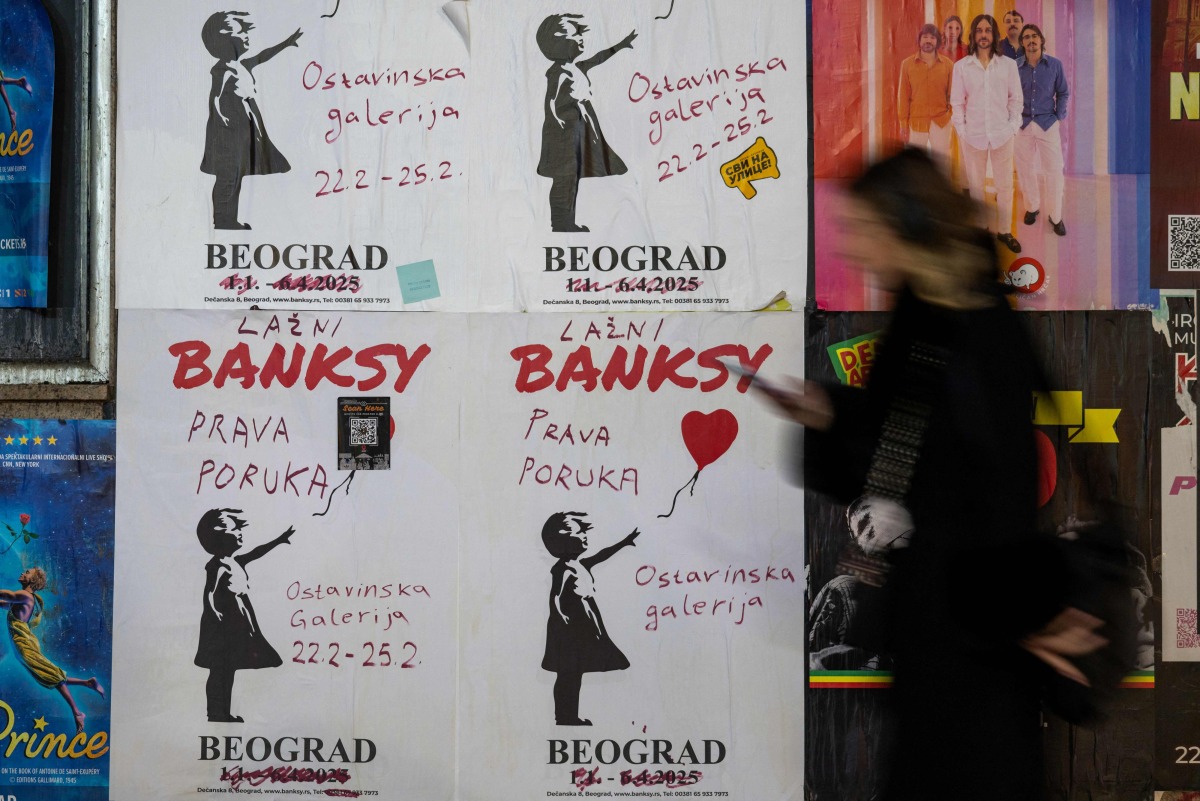 A woman walks past a poster advertising a gallery where an alternative and free exhibition showcases the work of the famous elusive artist Banksy in Belgrade on February 25, 2025. Photo by Andrej ISAKOVIC / AFP