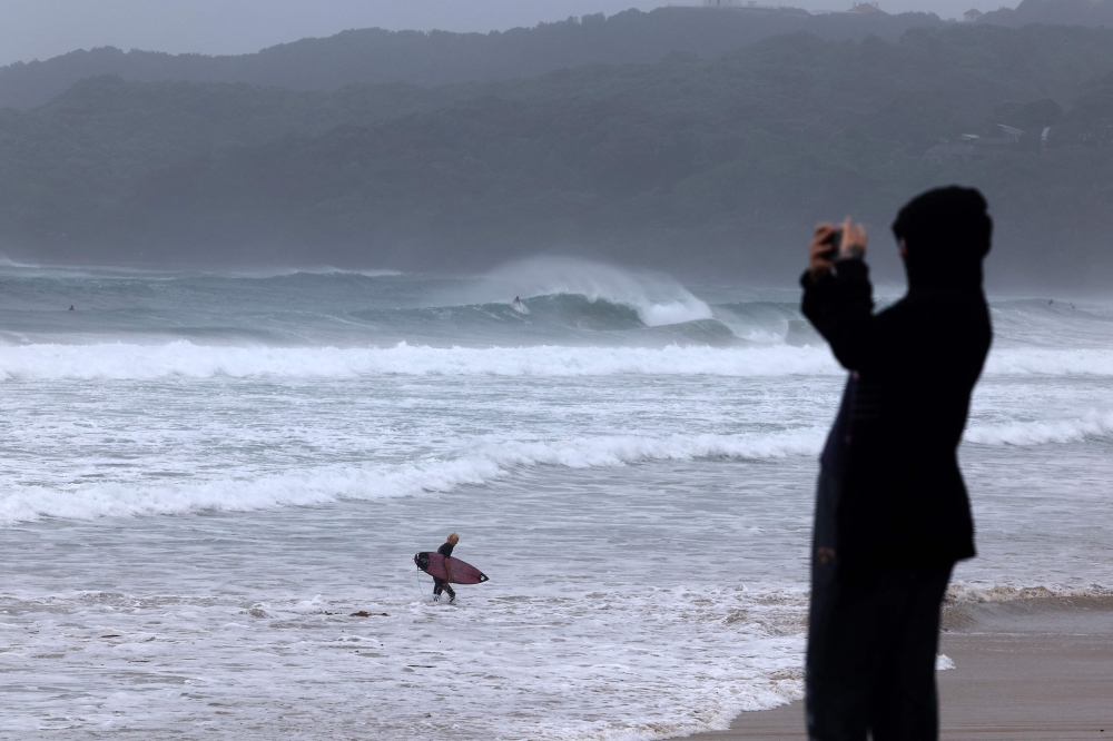 A resident takes pictures with a mobile phone of massive waves stirred by tropical cyclone Alfred at Byron Bay's Main Beach on March 5, 2025. (Photo by David Gray / AFP)