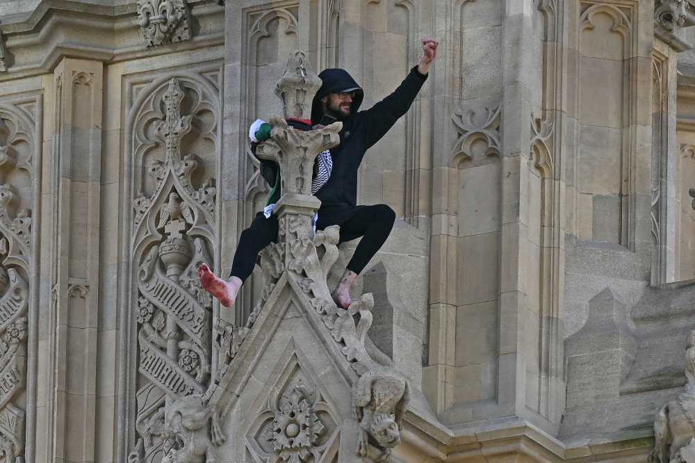 A protester holding a Palestinian flag gestures from the side of the Elizabeth Tower, commonly known by the name of the clock's bell 
