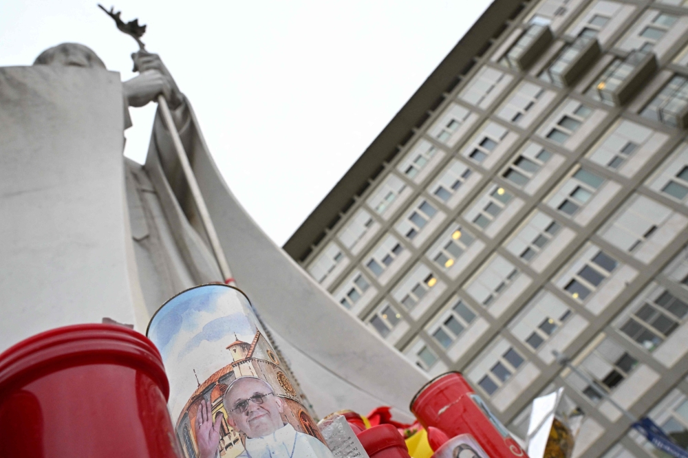 Candles are laid at the statue of John Paul II outside the Gemelli hospital where Pope Francis is hospitalized with pneumonia, in Rome on March 14, 2025. (Photo by Alberto Pizzoli / AFP)