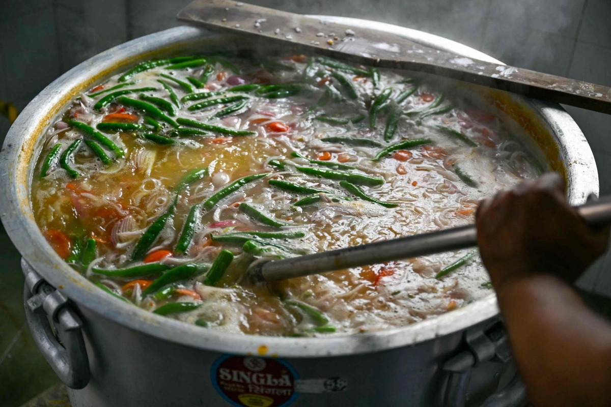 This picture taken on March 5, 2025 shows a Muslim man mixing ingredients to prepare the popular dish 'Bubur Lambuk' at Masjid India during the Muslim holy fasting month of Ramadan in Kuala Lumpur. (Photo by Mohd RASFAN / AFP)
