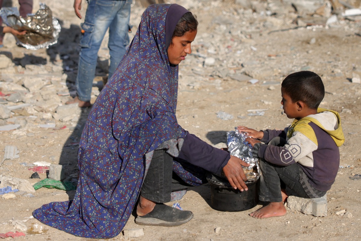 A woman and a boy cover a pot filled with food they received after queueing with others for charity meals given out during the Muslim holy fasting month of Ramadan in Gaza City on March 22, 2025. Photo by BASHAR TALEB / AFP