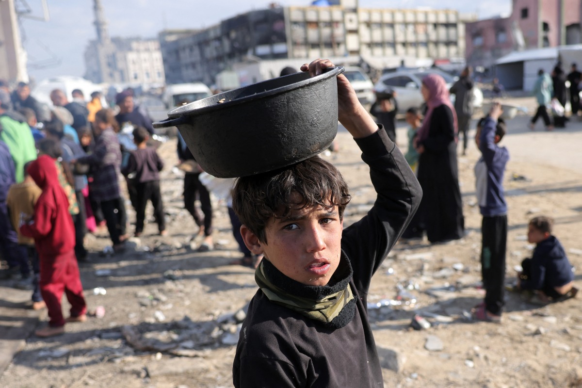 A boy walks with a pot of food he received after queueing for charity meals given out during the Muslim holy fasting month of Ramadan, in Gaza City on March 22, 2025. Photo by BASHAR TALEB / AFP