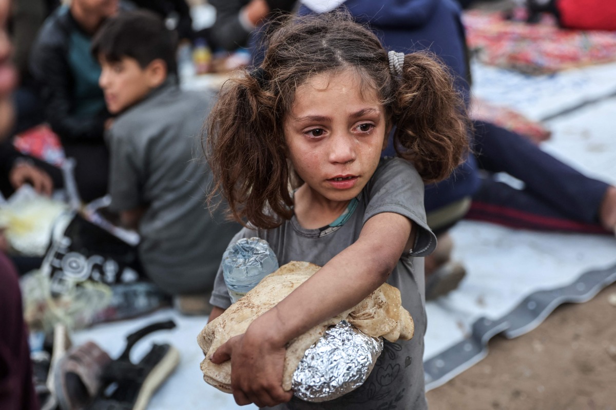A Palestinian child carrying food cries as people gather for a mass fast-breaking iftar meal in Beit Lahia in the northern Gaza Strip on March 15, 2025. (Photo by Omar Al-Qattaa / AFP)