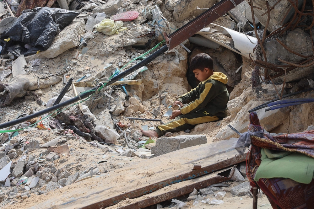 A Palestinian boy plays amidst the debris of a building destroyed during the Israel-Hamas war, in Gaza City on March 28, 2025. (Photo by Omar Al-Qattaa / AFP)