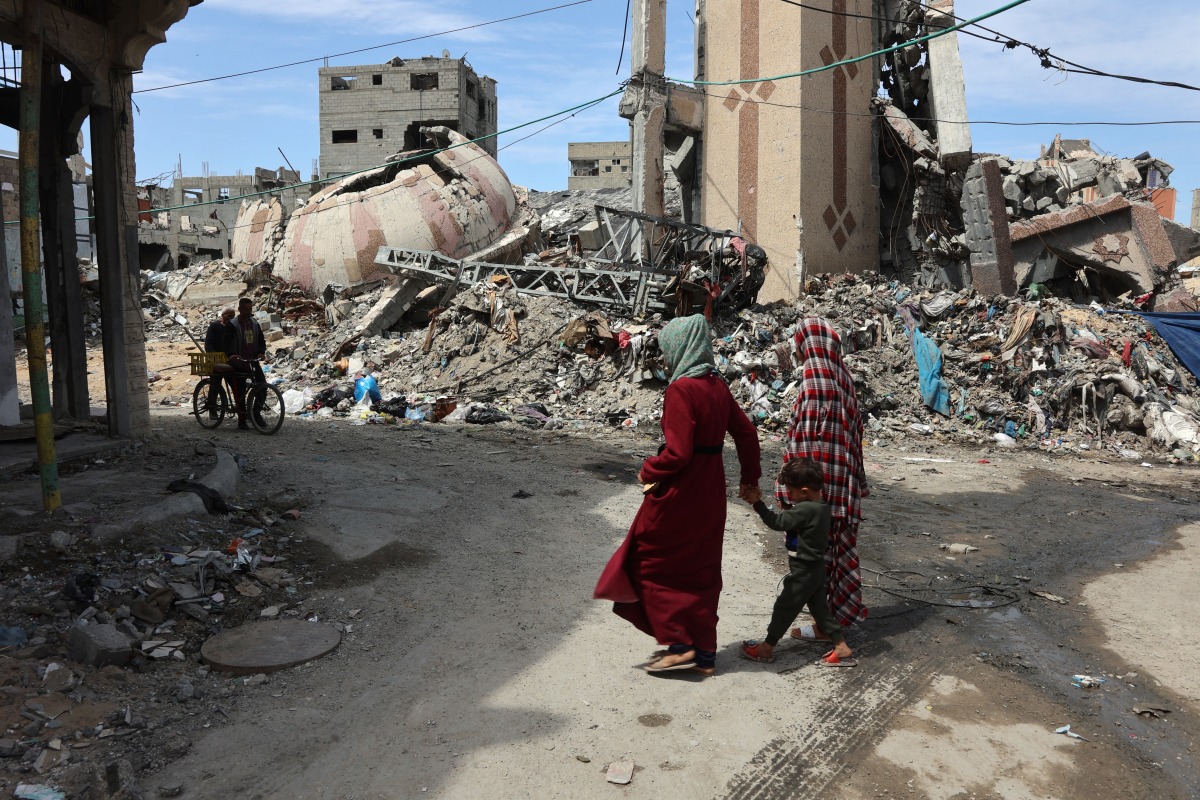 Palestinians walk past debris of buildings destroyed during the aggression in Gaza City on March 28, 2025. Photo by Omar AL-QATTAA / AFP.
