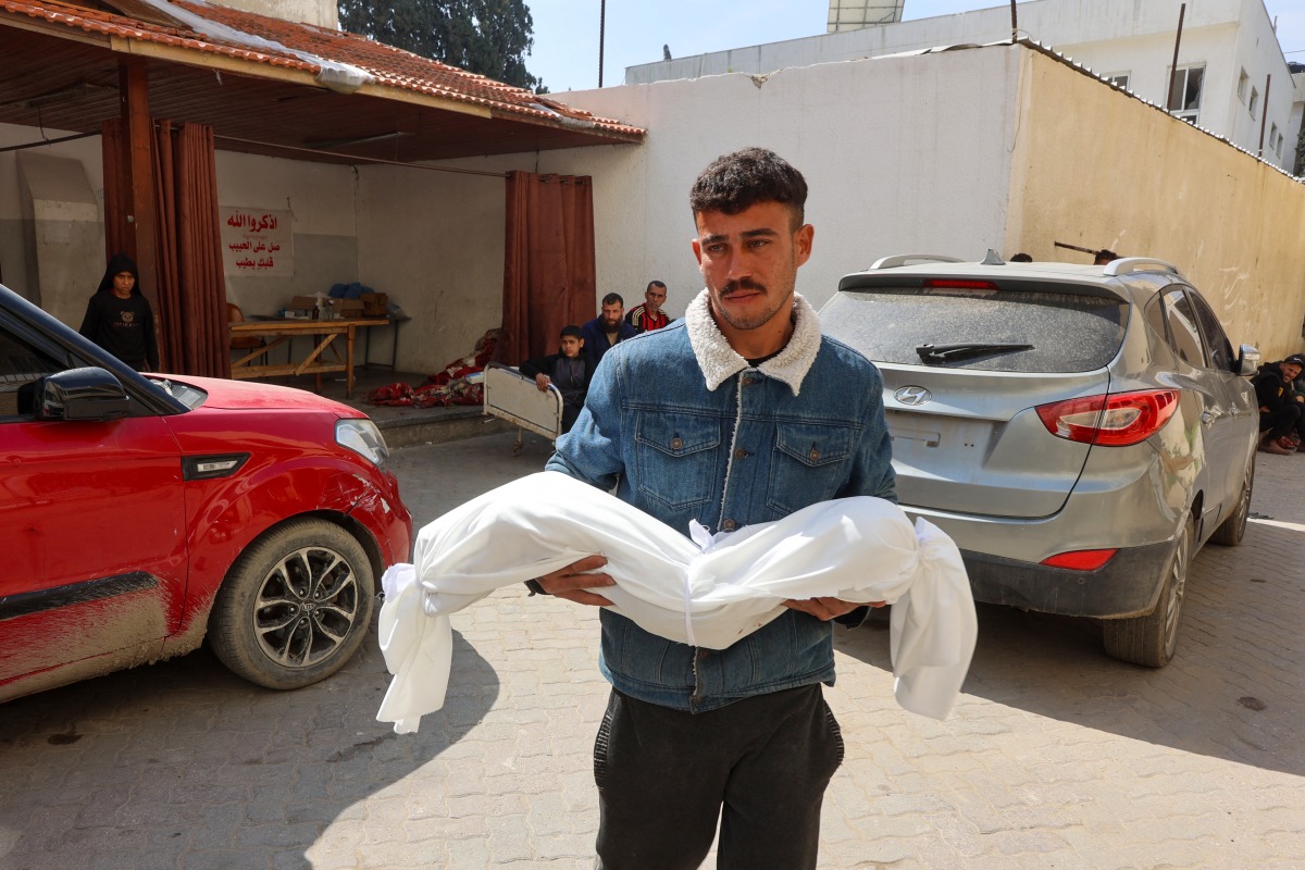 A man carries the body of a child, who was killed in an Israeli bombardment, at Al-Ahli Arab Hospital in Gaza City on March 26, 2025. Photo by Omar AL-QATTAA / AFP.