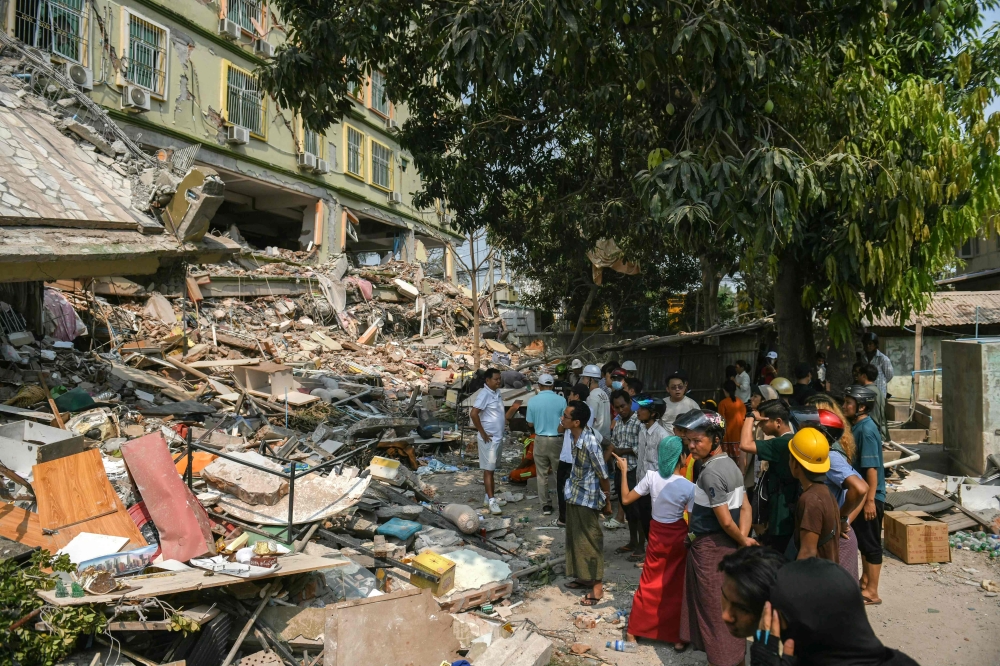People look on as teams of rescue workers attempt to free residents trapped under the rubble of the destroyed Sky Villa Condominium development in Mandalay on March 29, 2025. (Photo by Sai Aung Main / AFP)