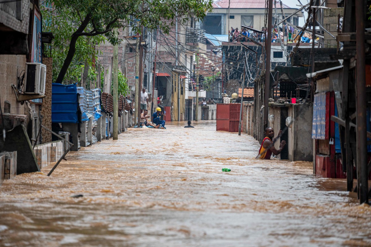 A resident wades through murky floodwaters following heavy rains in the Ndjili district of Kinshasa on April 6, 2025. Photo by Hardy BOPE / AFP