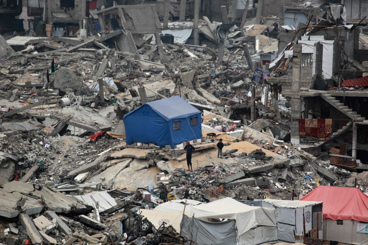 People stand outside their tent set up on the rubble of a destroyed building at the Jabalia camp for displaced Palestinians in the northern Gaza Strip on April 8, 2025. Photo by Bashar TALEB / AFP