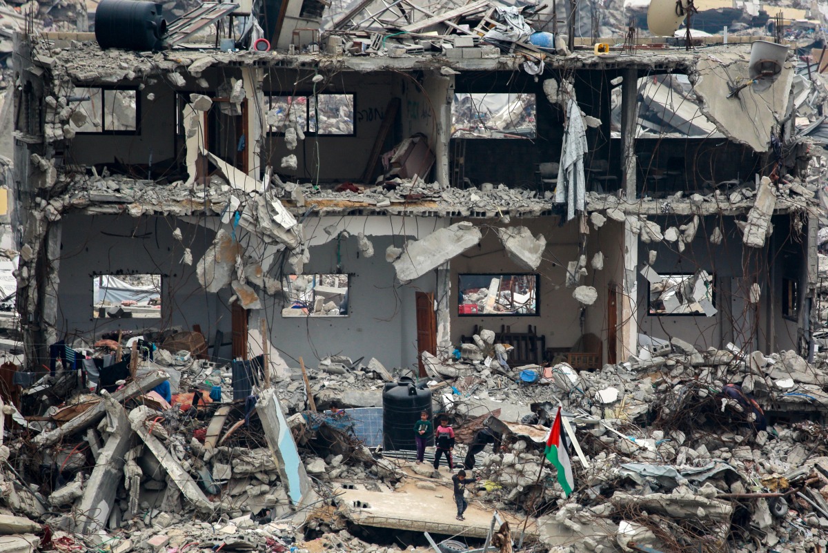 A Palestinian flag flutters as children play amid the rubble of a destroyed building at the Jabalia camp for displaced Palestinians in the northern Gaza Strip on April 8, 2025. Photo by Bashar TALEB / AFP
