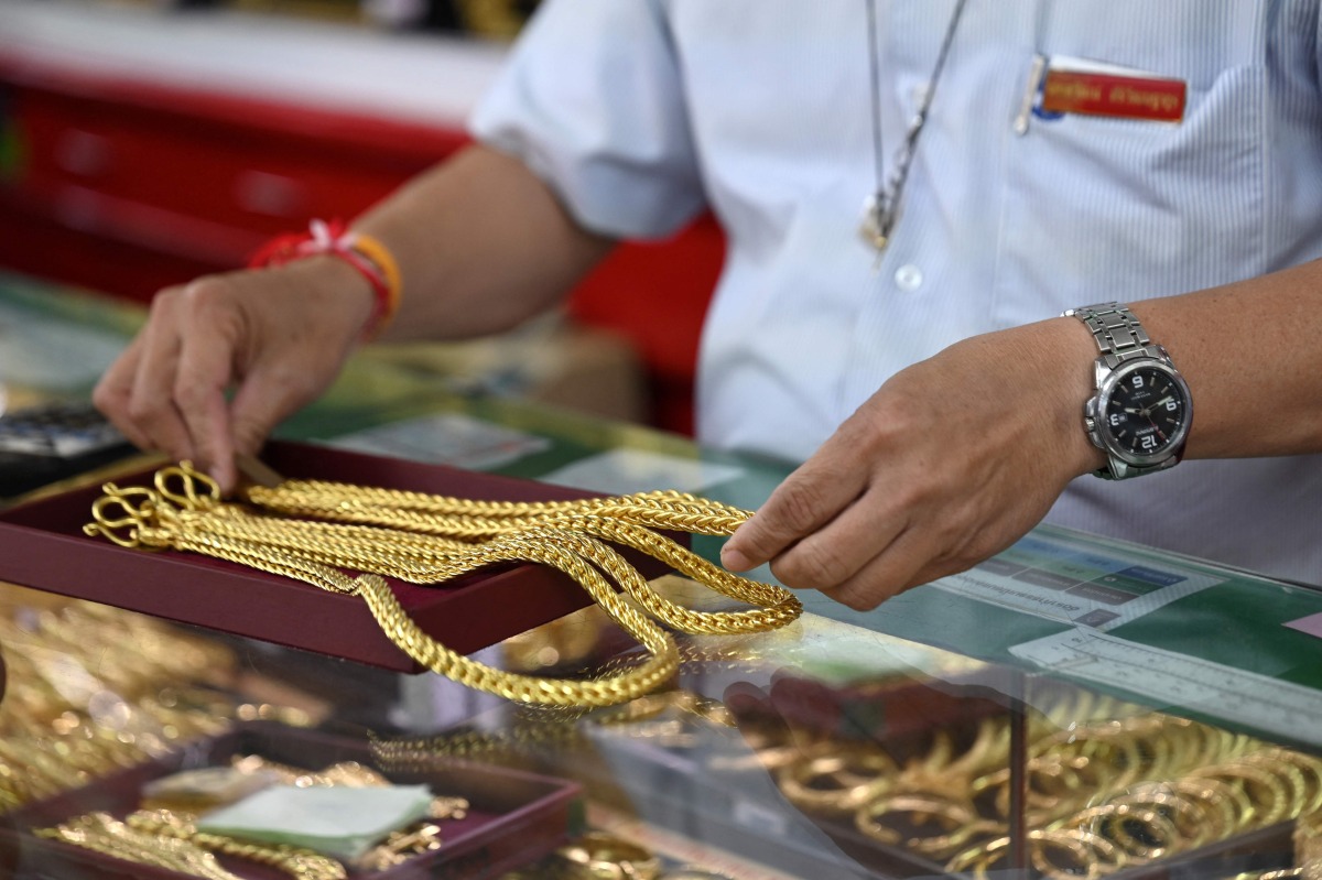 An employee handles gold jewelry for customers at Hua Seng Heng gold traders in Chinatown in Bangkok on April 9, 2025. (Photo by Lillian SUWANRUMPHA / AFP)
