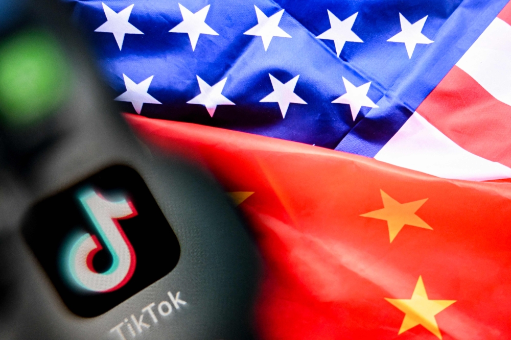 A photo taken on April 10, 2025 shows the Chinese social networking service TikTok's logo on a smartphone screen and US' and China flags combo illustration on a laptop screen in Frankfurt am Main, western Germany. (Photo by Kirill Kudryavtsev / AFP)

