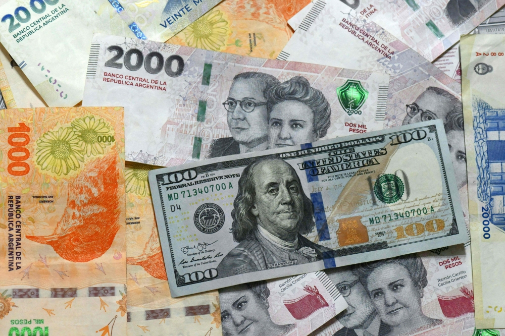 This photo illustration shows 20,000 Argentinian pesos, 2,000 Argentinian pesos, 1,000 Argentinian pesos, and 100 US dollar banknotes in Buenos Aires on April 11, 2025. (Photo by Luis Robayo / AFP)