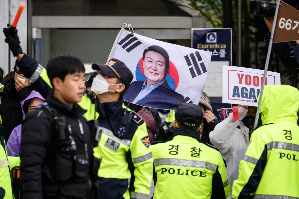 Police stand in front of pro-Yoon supporters on the side of a road as they wait for the arrival of former South Korean president Yoon Suk Yeol (pictured on flag) outside the Central District Court in Seoul on April 14, 2025. Photo by ANTHONY WALLACE / AFP