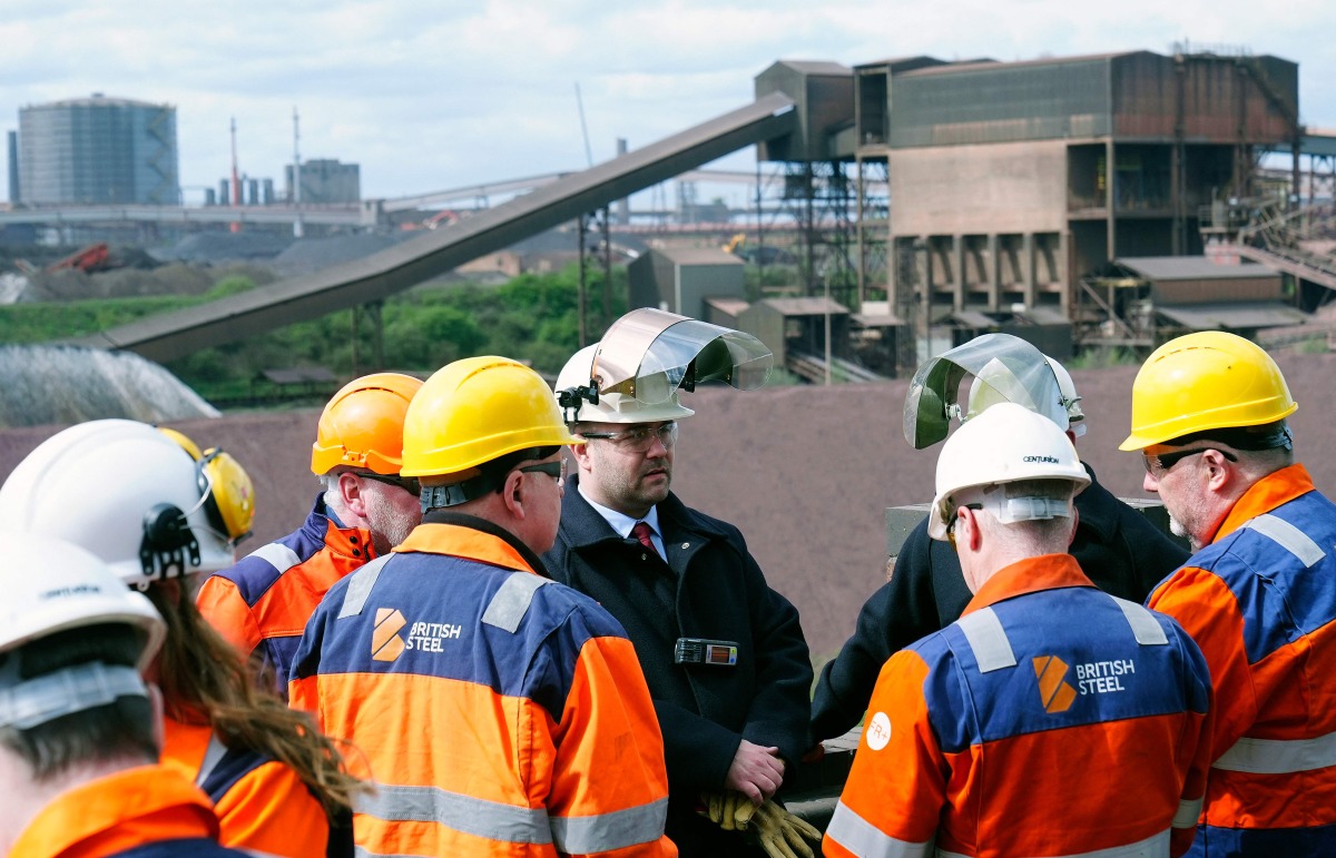 British Steel staff members talk before posing for a photograph with Britain's Deputy Prime Minister Angela Rayner (unseen) with the blast furnaces in the background, during her visit to British Steel's site in Scunthorpe, northern England on April 14, 2025. (Photo by Peter Byrne / POOL / AFP)
