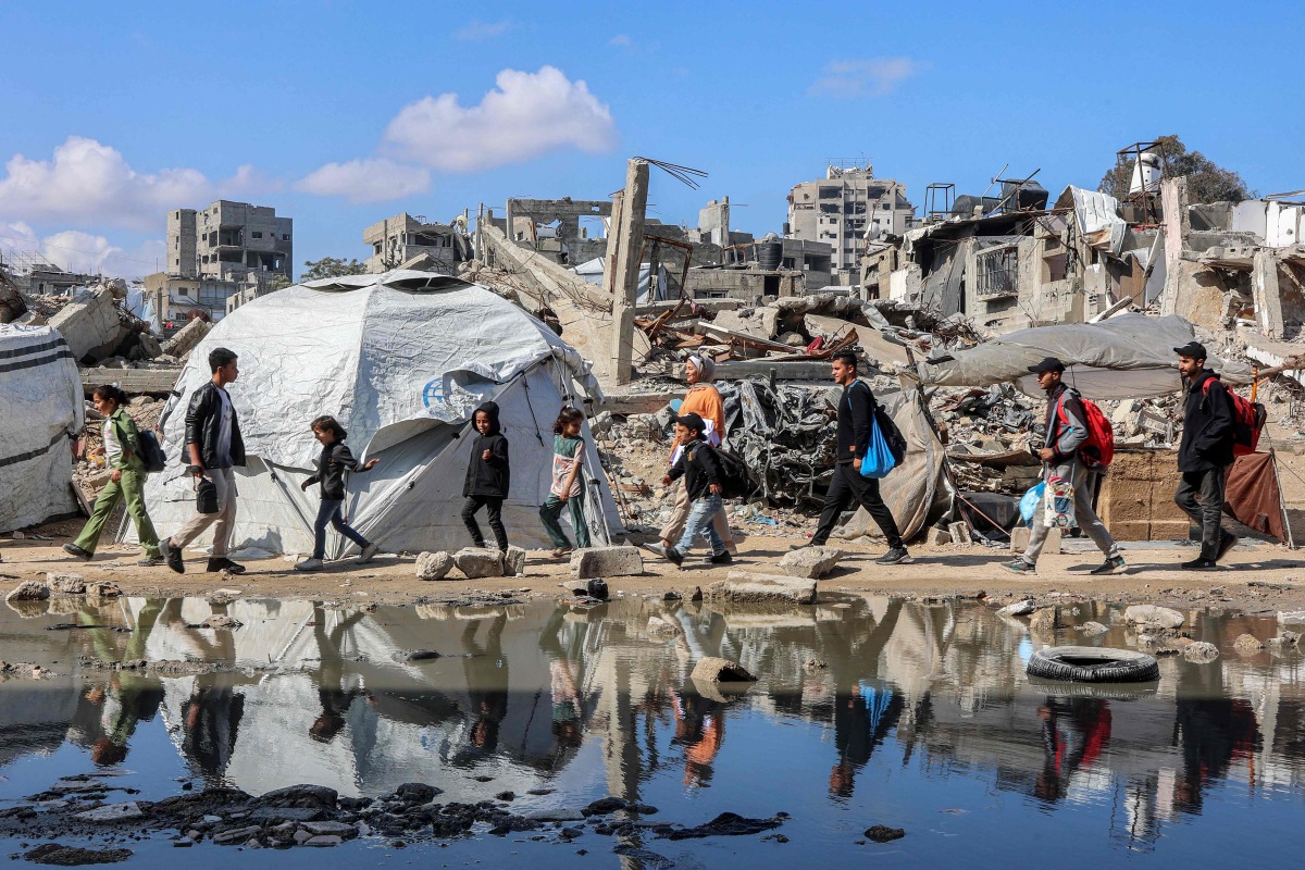  People walk past a puddle of water by a tent shelter erected near the rubble of a collapsed building in the Nasr neighbourhood in western Gaza City on April 15, 2025. Photo by Omar AL-QATTAA / AFP