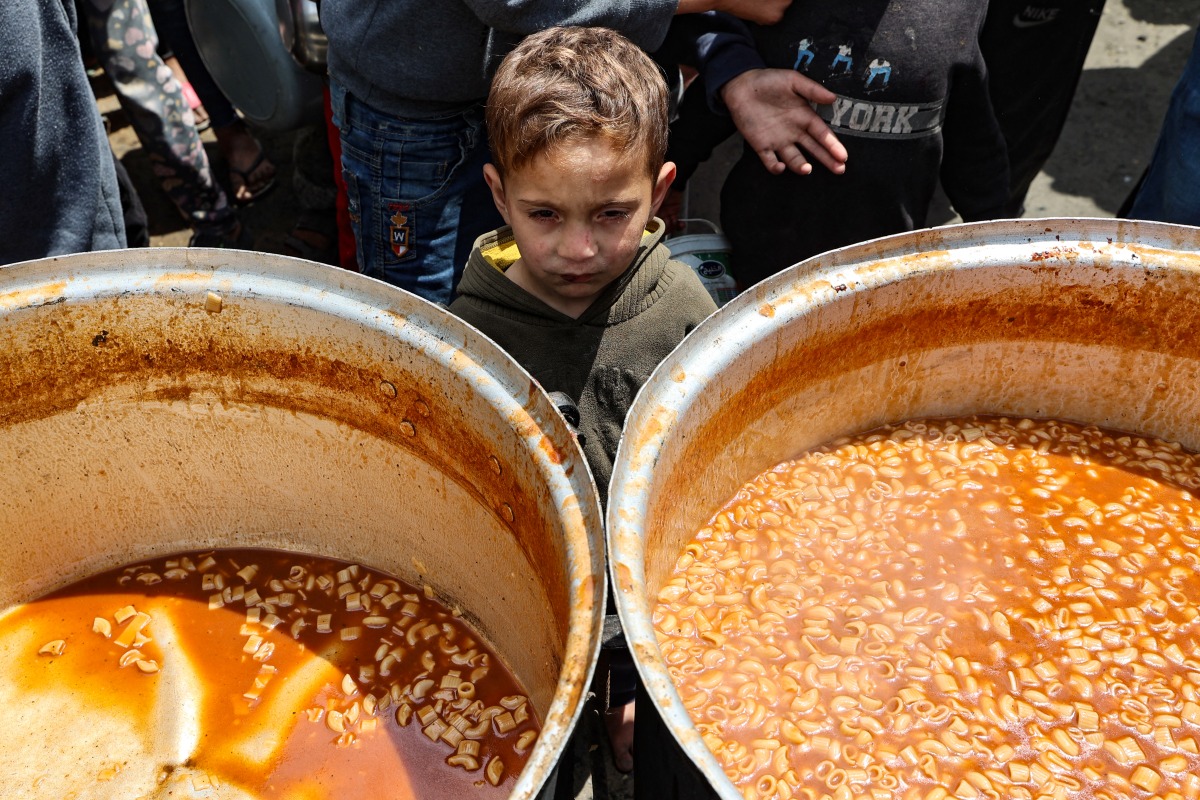 A Palestinian child waits to receive his portion of food a distribution point at the Nuseirat refugee camp in the central Gaza Strip on April 12, 2025. Photo by Eyad BABA / AFP.