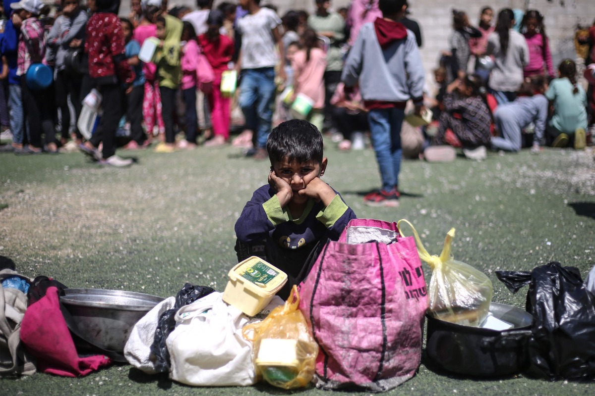 A Palestinian child waits to receive a hot meal at a free food distribution point at the Nuseirat refugee camp in the central Gaza Strip on April 19, 2025. (Photo by Eyad BABA / AFP)