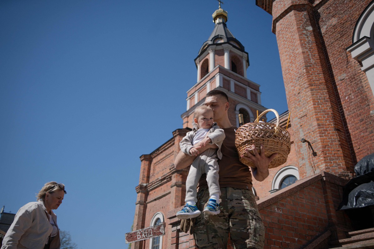 An Ukrainian serviceman holds his toodler and a basket with traditional Easter cakes and eggs during Easter service outside the Church of Ivan the Theologian, in Kharkiv, on April 20, 2025, amid the Russian invasion of Ukraine. (Photo by Ivan SAMOILOV / AFP)
