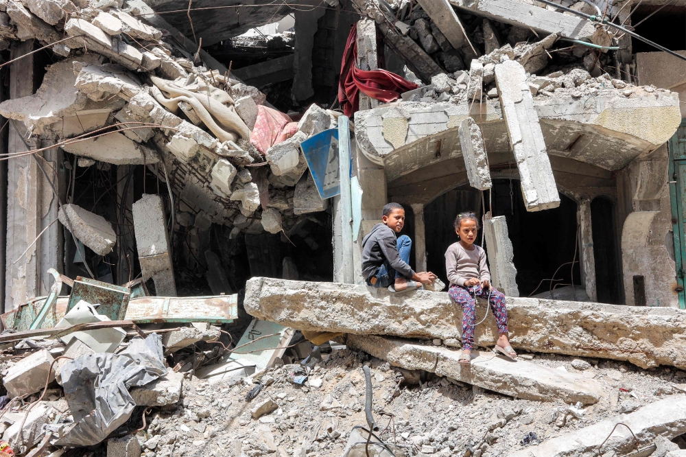A boy and girl sit by the ruins of a destroyed building in Gaza City on April 21, 2025. (Photo by Omar Al Qattaa / AFP)
