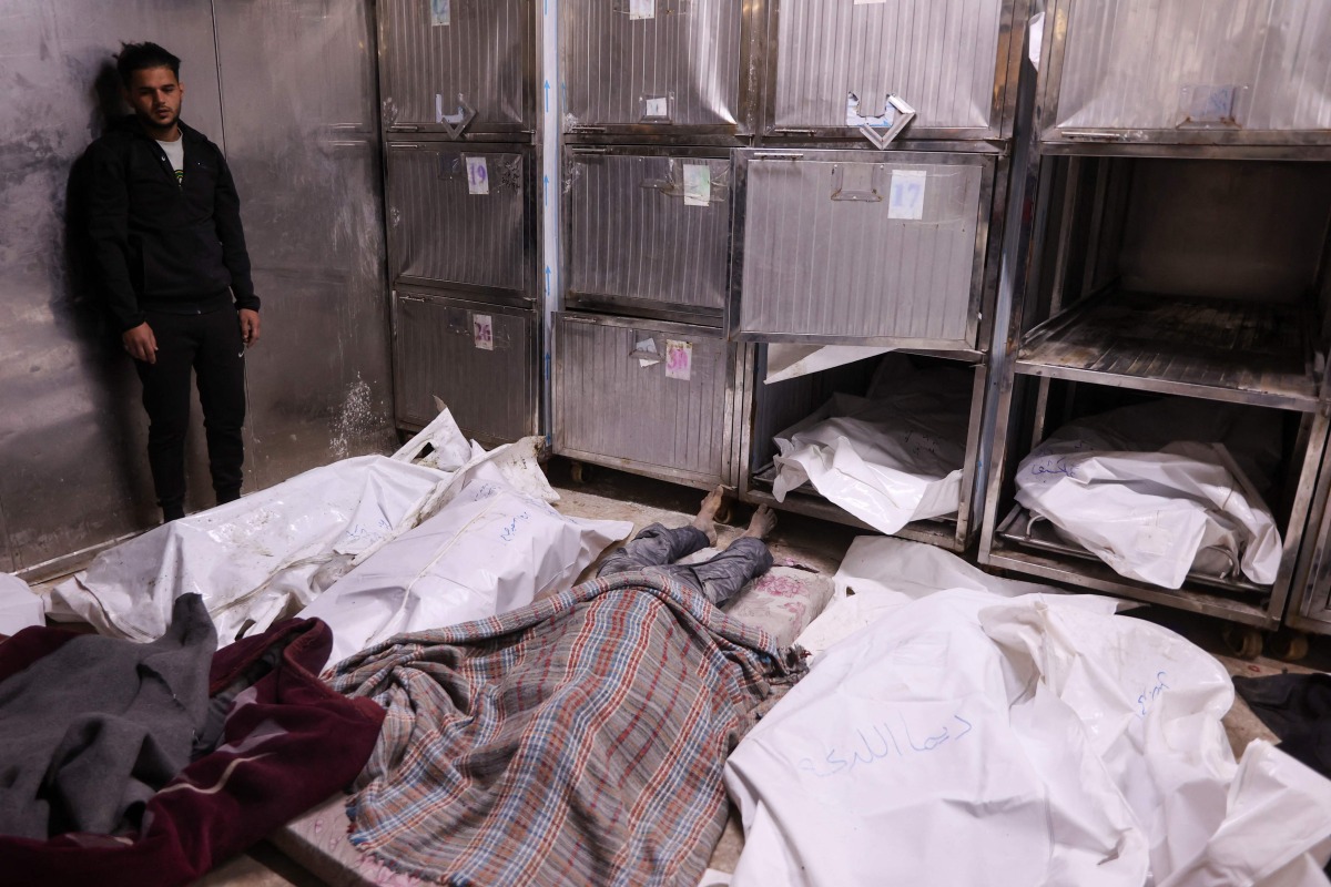 A Palestinian man stand over covered bodies, killed in an Israeli strike on a school-turned-shelter, at the morgue of the Al-Shifa hospital in Gaza City on April 23, 2025. Photo by Omar AL-QATTAA / AFP