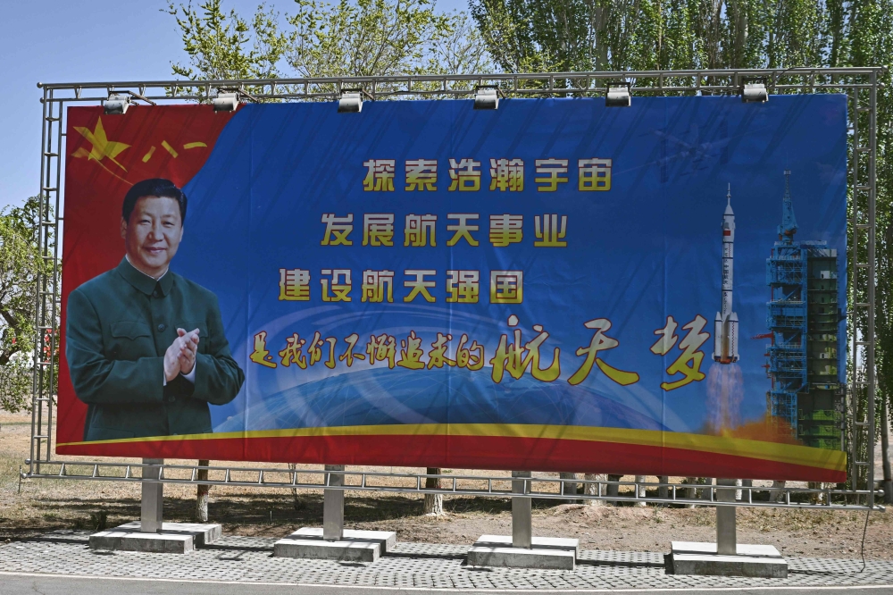 A poster of China's President Xi Jinping is seen beside a slogan referencing China's space ambitions at the Jiuquan Satellite Launch Centre in the Gobi desert in northwest China on April 23, 2025, a day before the launch of the Shenzhou-20 mission. (Photo by Pedro Pardo / AFP)
