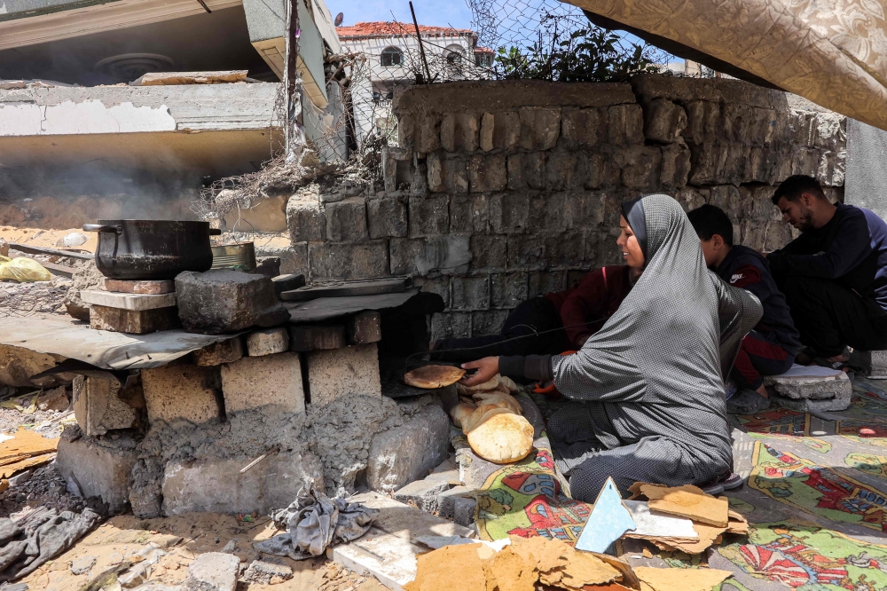 A woman bakes pita bread loaves in an oven by a tent in Gaza City on April 21, 2025. (Photo by Omar AL-QATTAA / AFP)