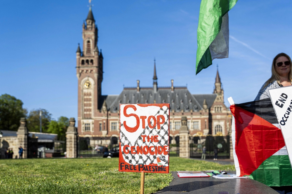A demonstrator stands beside a placad reading 