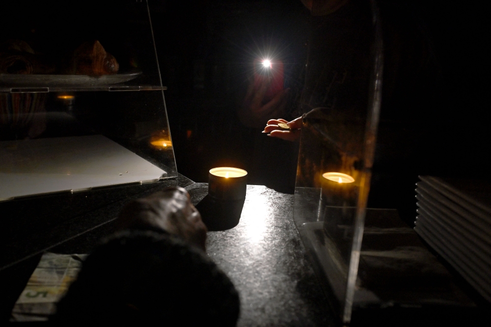 A waiter gives change by the light of her phone in a bar during a massive power cut affecting the entire Iberian peninsula and the south of France, in Hernani on April 28, 2025. (Photo by Ander Gillenea / AFP)