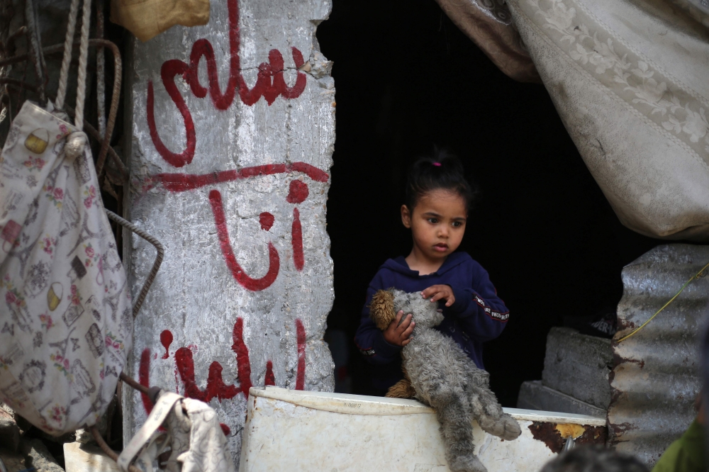 A girl stands near graffiti on a concrete pillar with names of Palestinian father Wissam Wishah's children, Said, Salma, and Eline who were killed in Israeli strikes in the vicinity of their home, at their heavily damaged house at the Al Bureij refugee camp in the central Gaza Strip on May 1, 2025. (Photo by Eyad Baba / AFP)
