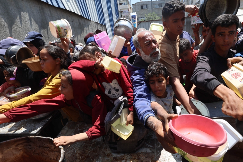 Palestinians queue for a hot meal at a charity kitchen at the Nuseirat refugee camp in the central Gaza Strip on May 4, 2025. (Photo by Eyad Baba / AFP)