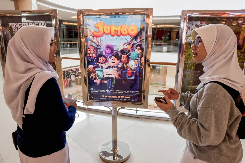 This picture taken on April 21, 2025 shows two teenagers speaking next to a poster of the animated film Jumbo at a cinema in Bekasi, West Java. (Photo by Bay Ismoyo / AFP) 