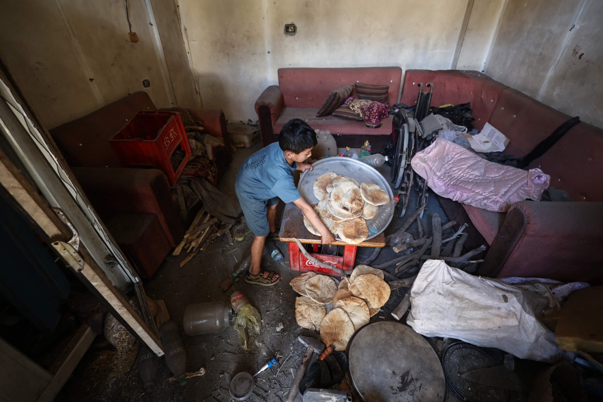 A Palestinian boy salvages bread from a makeshift bakery hit in Israeli strikes at the Nuseirat refugee camp in the central Gaza Strip on May 8, 2025. (Photo by Eyad BABA / AFP)