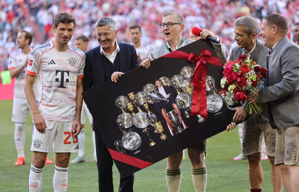 Bayern Munich's German forward #25 Thomas Mueller (L) is handed by Bayern Munich's President Herbert Hainer a picture showing Muller inmid trophies ahead the German first division Bundesliga football match between Bayern Munich and Borussia Moenchengladbach in Munich on May 10, 2025. (Photo by Alexandra BEIER / AFP)