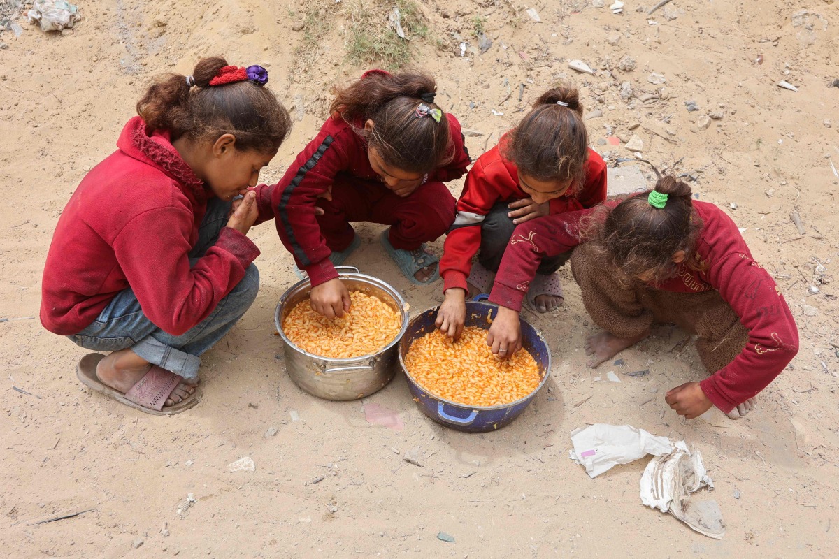 Palestinian girls eat hot food from rations provided at a charity kitchen set up at the Islamic University campus in Gaza City on May 12, 2025. (Photo by Omar AL-QATTAA / AFP)
