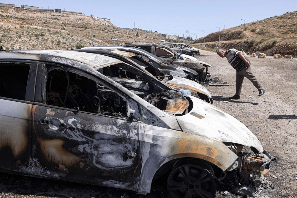 A Palestinian man looks at burnt out vehicles in the Barkan Industrial area, near Salfit in the occupied West Bank on May 16, 2025. (Photo by Jaafar Ashtiyeh / AFP)