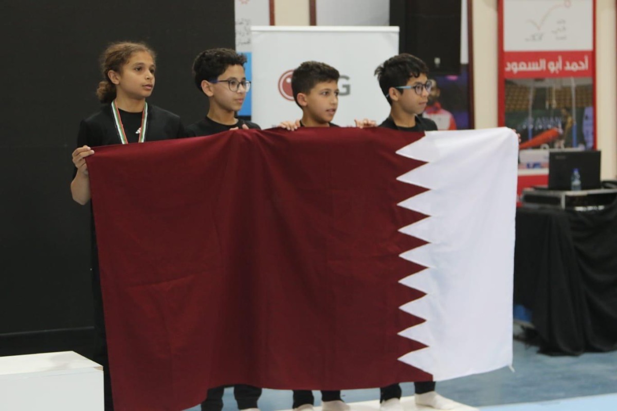 Young Qatar gymnasts celebrate with the national flag after securing bronze at the West Asian Championship.