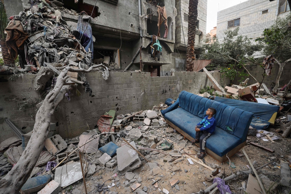A Palestinian boy sits on a damaged couch as he watches people clearing the rubble from a house hit in Israeli strikes at the Nuseirat refugee camp. (Photo by Eyad BABA / AFP)