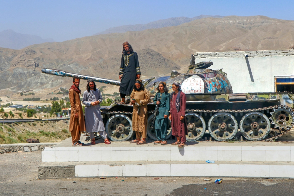 Taliban security personnel pose on a Soviet tank along a road in Surobi district, Kabul province on May 20, 2025. (Photo by MOHAMMAD FAISAL NAWEED / AFP)
