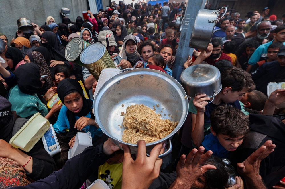 Palestinians gather to receive a hot meal at a food distribution point in the Nuseirat camp for refugees in the central Gaza Strip on May 21, 2025. (Photo by Eyad Baba / AFP)