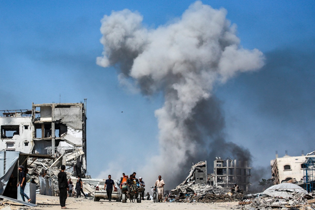 People move past destroyed buildings as smoke billows following an Israeli strike in Jabalia, in the northern Gaza Strip on May 25, 2025. (Photo by Bashar Taleb / AFP)
