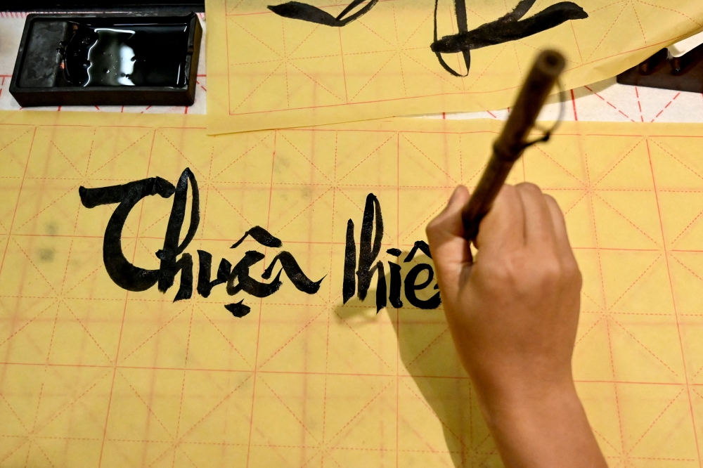 This photo taken on May 15, 2025 shows Hoang Thi Thanh Huyen learning calligraphy at the home of calligrapher Nguyen Thanh Tung in Hanoi. (Photo by Nhac Nguyen / AFP) / 