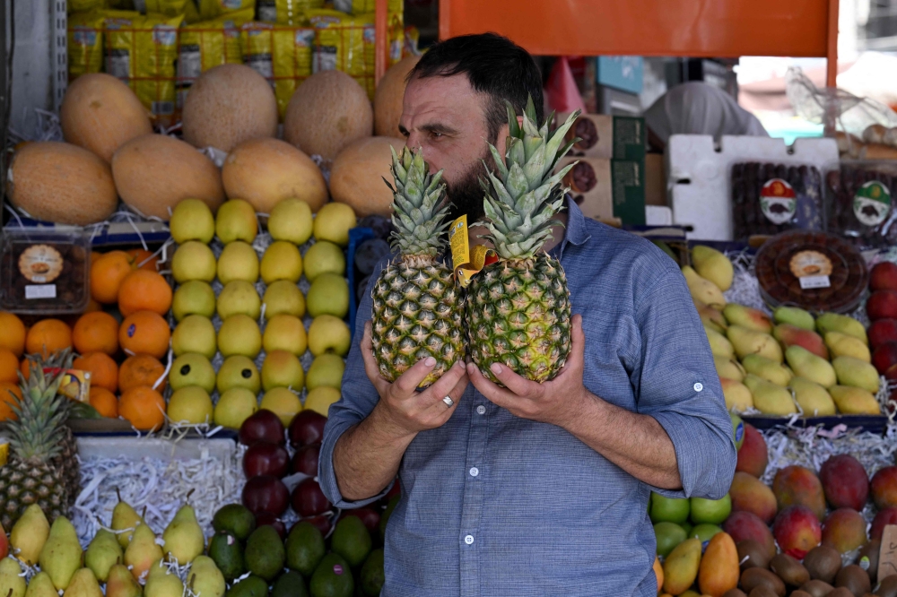 A man holds two pineapples at a stall that sells fruits in the Shalaan Market in the Syrian capital Damascus on May 26, 2025. (Photo by Louai Beshara / AFP)