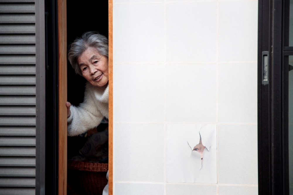 (Files) This file picture taken on January 16, 2018 shows Kimiko Nishimoto posing next to a picture of her on the sliding window of her house. (Photo by Behrouz Mehri / AFP)